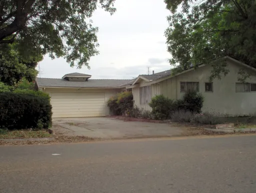 Ranch house before — dated beige siding, overgrown shrubs, worn driveway